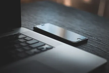 Smartfon obok laptopa na drewnianym biurku, test na różnych urządzeniach